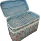 The Walker Valentine Walton Travel Case, featuring a floral pattern and double zippers, is open on a woven surface to reveal spacious, clear plastic-lined compartments.