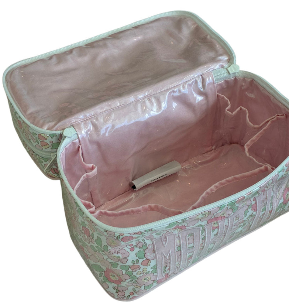 The Walton Travel Case by Walker Valentine, a rectangular floral fabric organizer with a pink interior, is open to show inner pockets and a lighter inside.