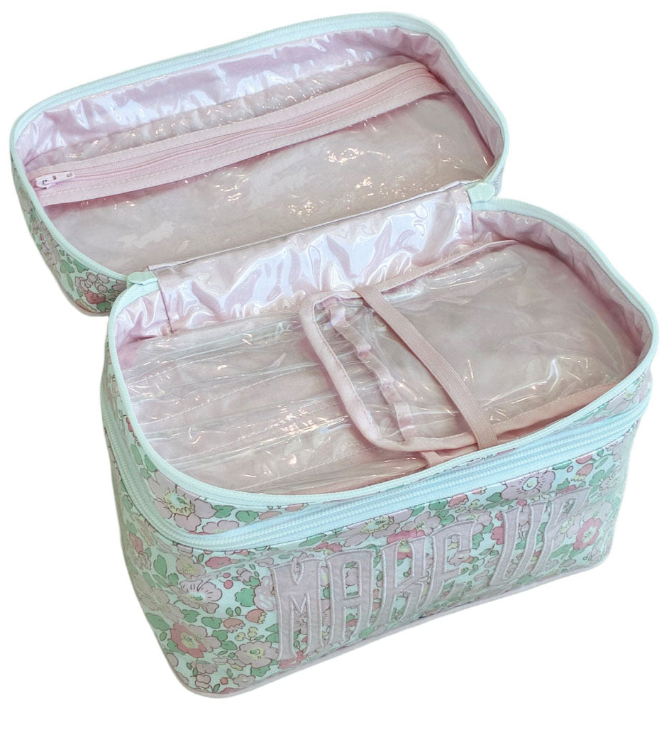 The Walton Travel Case by Walker Valentine is a pastel floral makeup bag with "MAKEUP" on the front, featuring multiple clear compartments inside—ideal for organizing your beauty essentials while traveling.