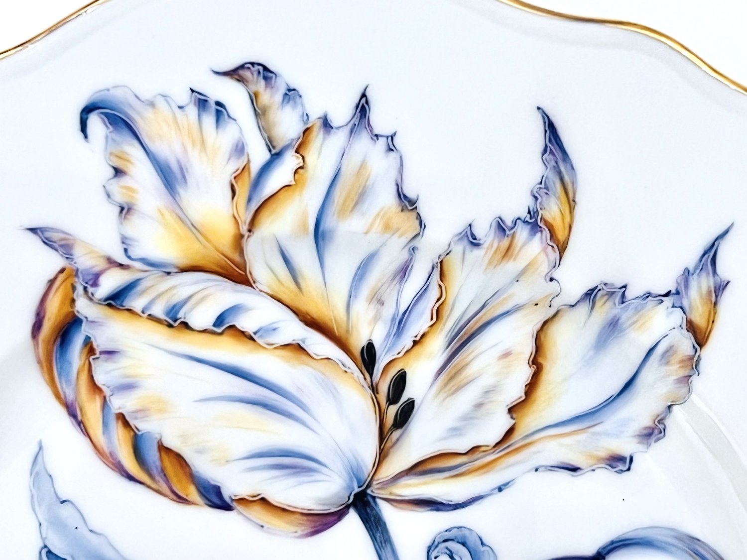 Close-up of the Botanical Treasures Salad Plate VI by Anna Weatherley, a white porcelain plate with intricate hand-painted yellow, blue, and purple floral details and a gold rim.