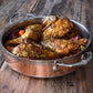 Herb-seasoned roast chicken pieces in the Hestan CopperBond Copper Induction Sauteuse, 3.5qt, sit atop roasted vegetables on a rustic wooden surface.