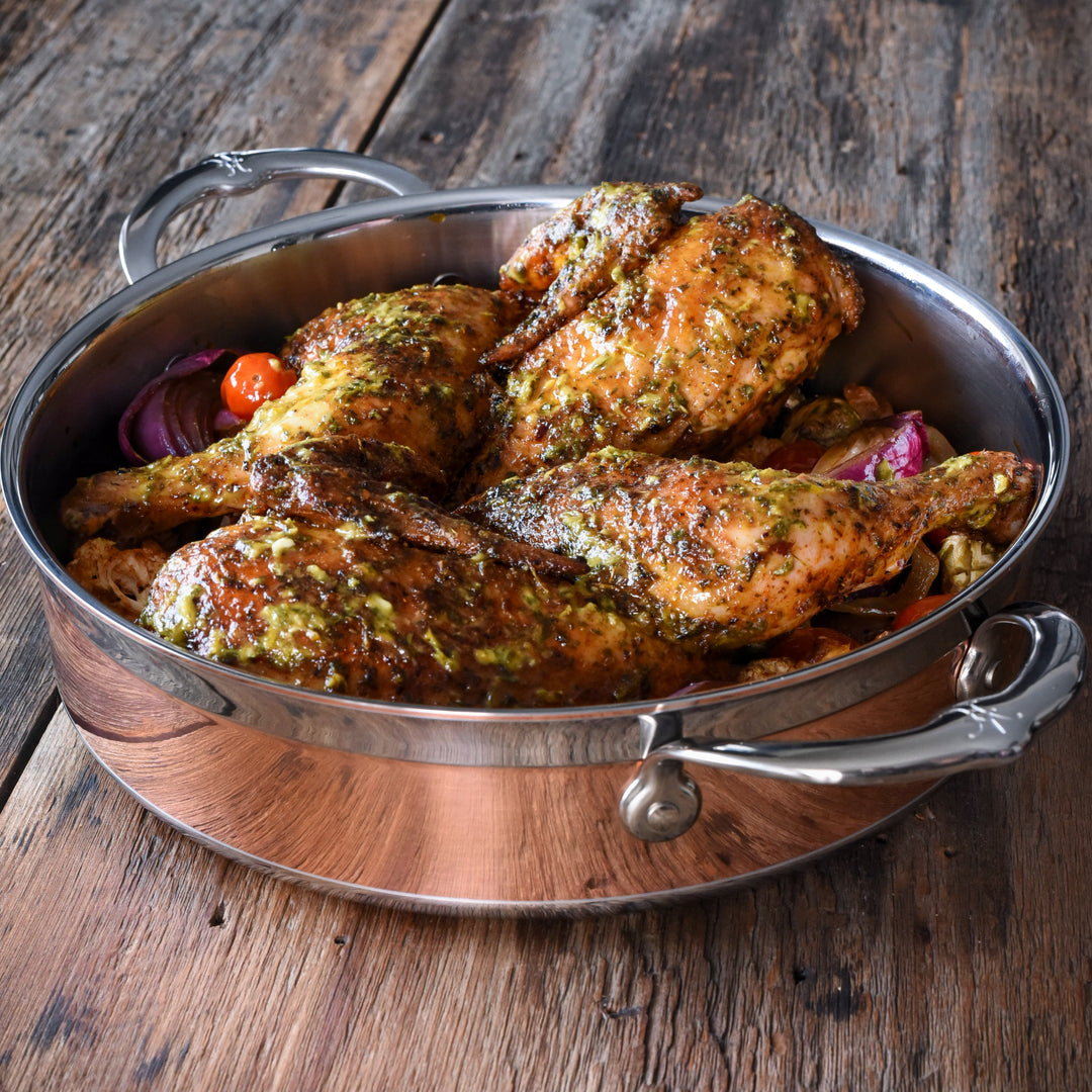 Herb-seasoned roast chicken pieces in the Hestan CopperBond Copper Induction Sauteuse, 3.5qt, sit atop roasted vegetables on a rustic wooden surface.