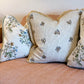 Three Flax Field Flower with Leaf Trim Pillows by Hive Custom Pillows, featuring floral patterns and fine materials, are arranged on a light pink upholstered sofa.