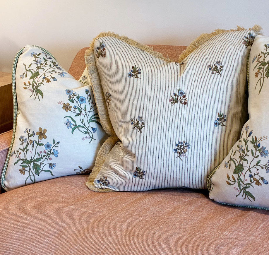 Three Flax Field Flower with Leaf Trim Pillows by Hive Custom Pillows, featuring floral patterns and fine materials, are arranged on a light pink upholstered sofa.