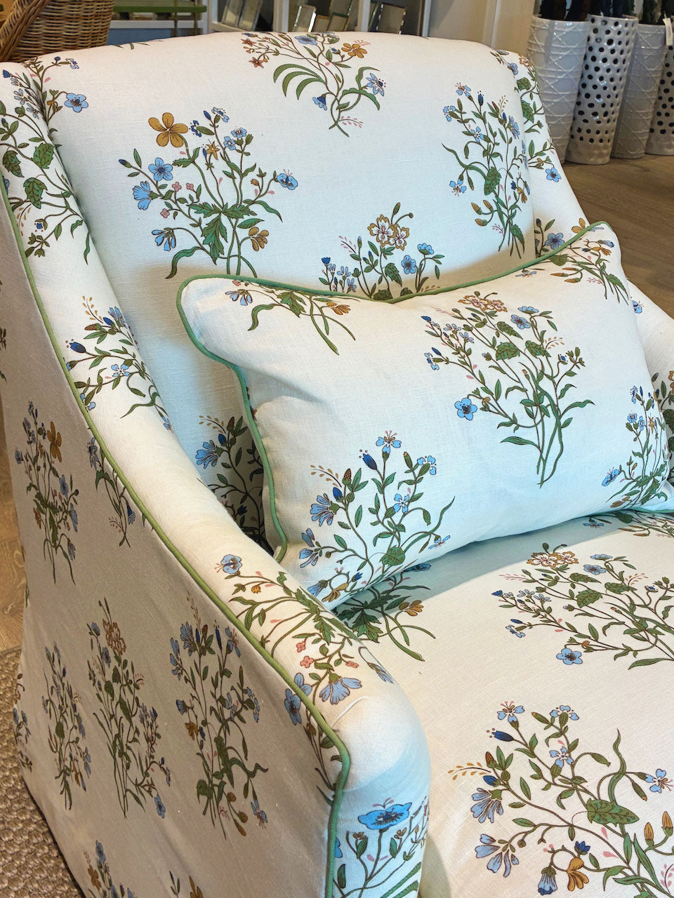 The Bowen Arm Chair in Flax & Field Flowers by Bunny Williams is an upholstered armchair with a matching pillow, both featuring a floral print on a light background and finished with elegant slipcover upholstery.