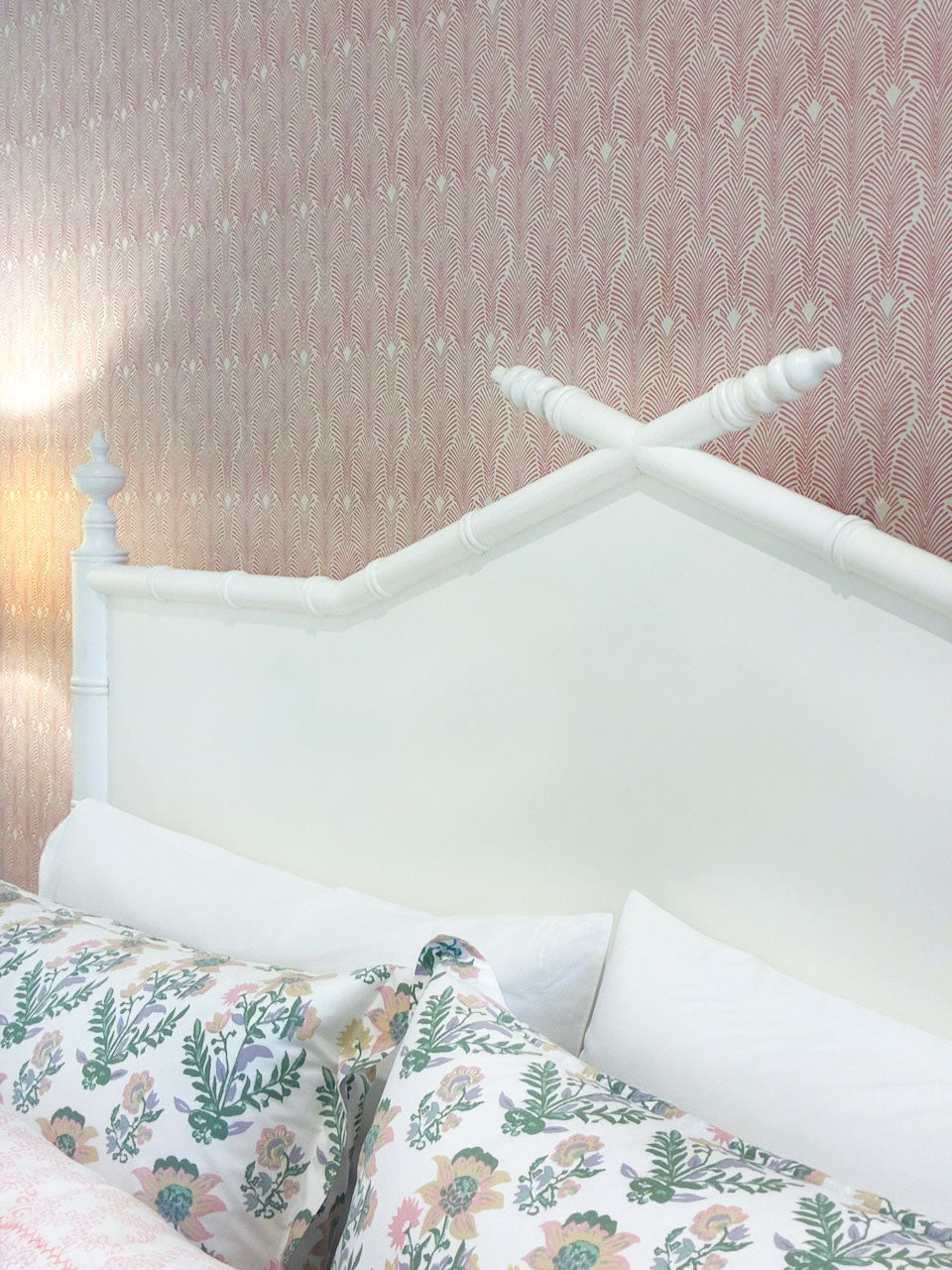The Bambu King Bed by Sherrill/Mr & Mrs Howard features a white wooden headboard with crossed posts, standing out against pink patterned wallpaper and floral bedding for a timeless solid wood look.