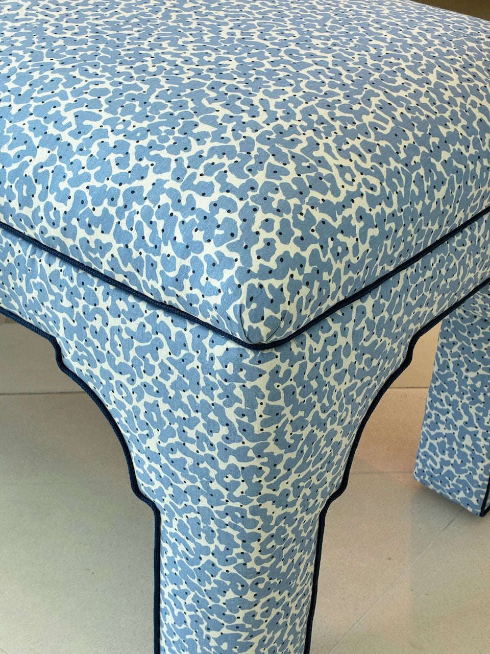 The Taj Bench by Bunny Williams features blue and white abstract upholstery, curved edges, dark seam piping, and elegant French nailhead trim for a refined look.