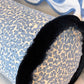 The Korallo Periwinkle Bolster Pillow by Hive Custom Pillows features a cylindrical blue and white pattern with black trim, shown in front of a white pillow with a blue wavy border.