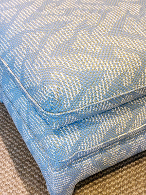 The Empire Ottoman in Blue Grande Gran by Bunny Williams, featuring a blue and white pattern, sits atop a textured beige surface, resembling a compact upholstered pouf.