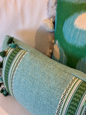 Two Pyla Lagon Pillows by Hive Custom Pillows, featuring green and white patterns with tassels, rest on a light-colored textured fabric surface.