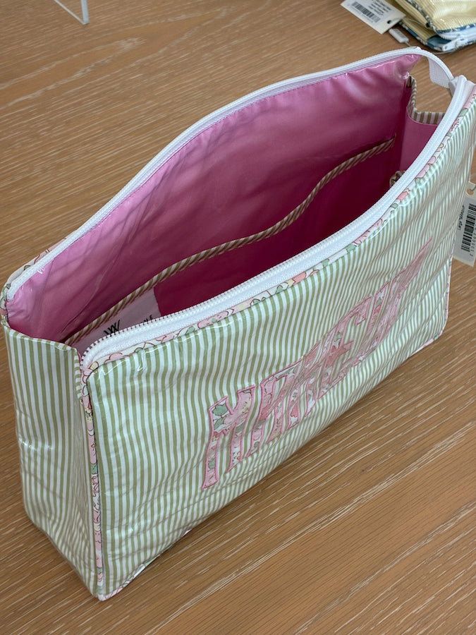 The Walker Valentine Large Helen Cosmetic Case, "MAKEUP," features green and white stripes, a pink interior, and small pockets. It is displayed on a wooden surface.