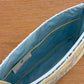 The Large Helen Cosmetic Case by Walker Valentine features a blue interior, multiple inner pockets, a "MAKEUP" label inside, and sits on a wooden surface—ideal for organizing cosmetics.