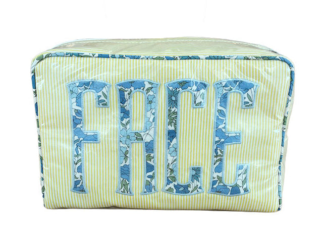 The Walker Valentine Large Milan Cosmetic Case, "FACE," is a rectangular zippered organizer with yellow stripes and bold blue floral letters—ideal as a stylish travel makeup bag.