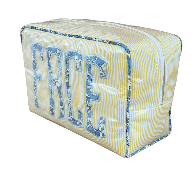 The Large Milan Cosmetic Case by Walker Valentine features yellow and white stripes with "FACE" in large blue patterned letters—a stylish zippered travel makeup bag and beauty organizer.