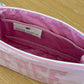 Open pink and white striped Small Helen Cosmetic Case, "FACE" by Walker Valentine, with the brand label sewn inside, placed on a wooden surface.
