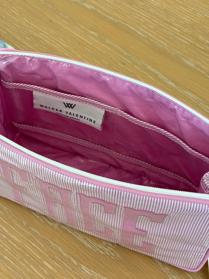 Open pink and white striped Small Helen Cosmetic Case, "FACE" by Walker Valentine, with the brand label sewn inside, placed on a wooden surface.