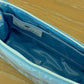 The Small Helen Cosmetic Case "FACE" by Walker Valentine features blue and white stripes, a zippered closure, blue interior, and label—perfect for travel and cosmetics. Shown here on a wooden surface.