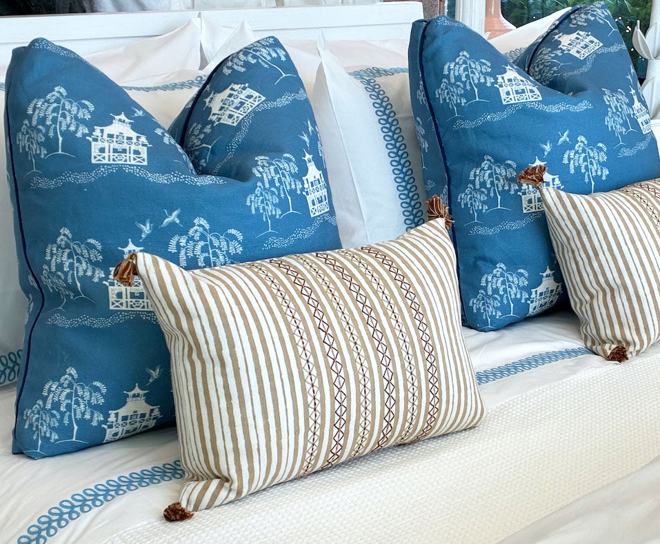 Three decorative pillows by Hive Custom Pillows are on the bed: two large Fall Pagoda Blue Pillows with white scenic patterns, and one smaller striped pillow featuring tassels.