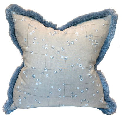 The Klimt Grid Pillow with Sky Brush Fringe by Associated Design features light beige fabric with a blue abstract dot pattern and blue fringed edges—a luxurious decorative accent for any space.