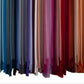 Rows of fabric swatches from the Alicia Adams Alpaca Classic Throw Collection hang vertically in a gradient—from blues and grays on the left to pinks, reds, and oranges on the right.