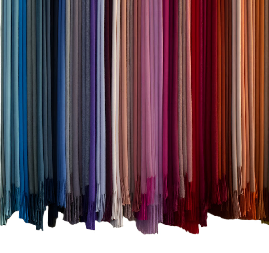 Rows of fabric swatches from the Alicia Adams Alpaca Classic Throw Collection hang vertically in a gradient—from blues and grays on the left to pinks, reds, and oranges on the right.