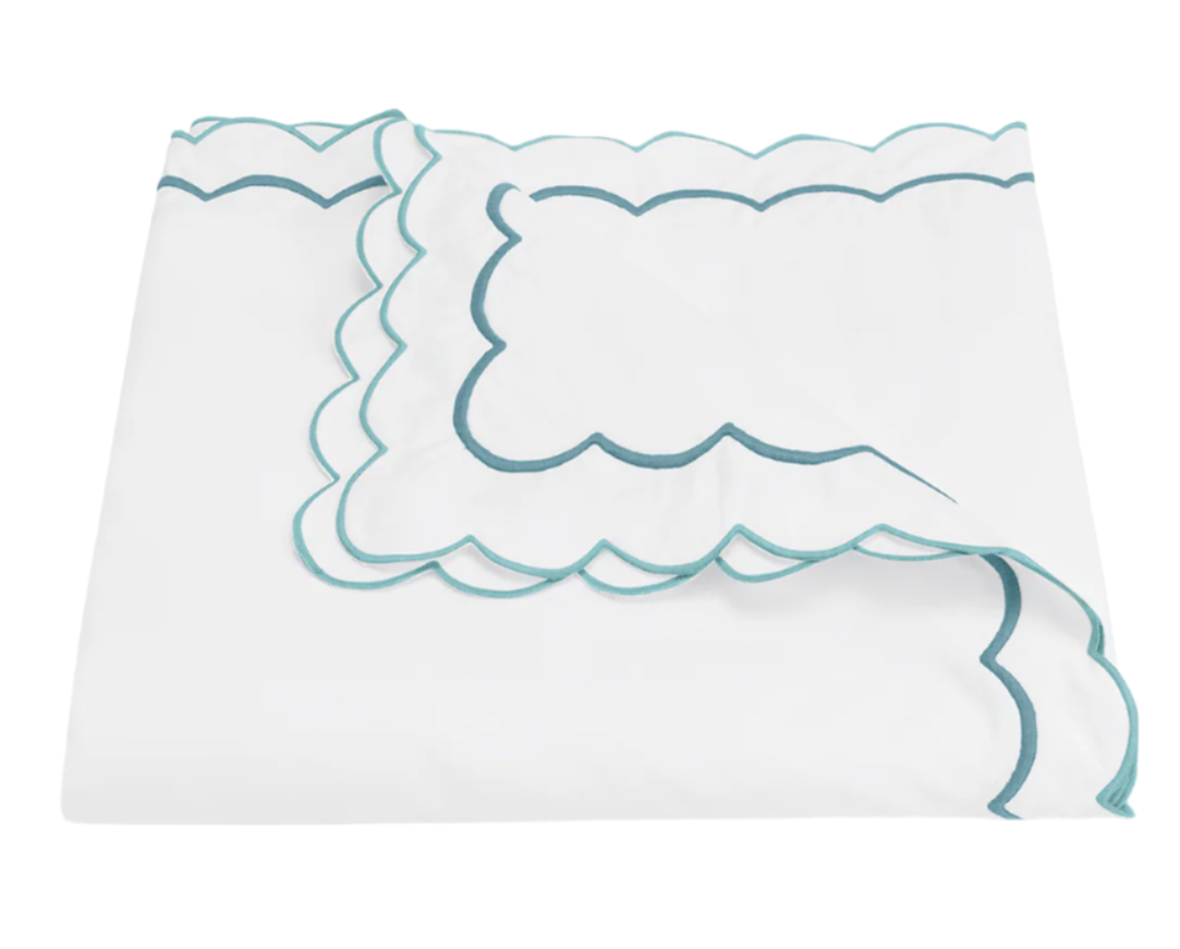The India Bedding Collection, Cerulean by Matouk features a folded white cotton percale bedsheet with teal scalloped embroidery, displayed on a plain white background and crafted to meet OEKO-TEX Standard 100 for safety and quality.