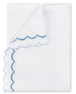 A folded white towel from the Matouk India Pique Bedding Collection in Azure features delicate double-scallop embroidery along the edges.