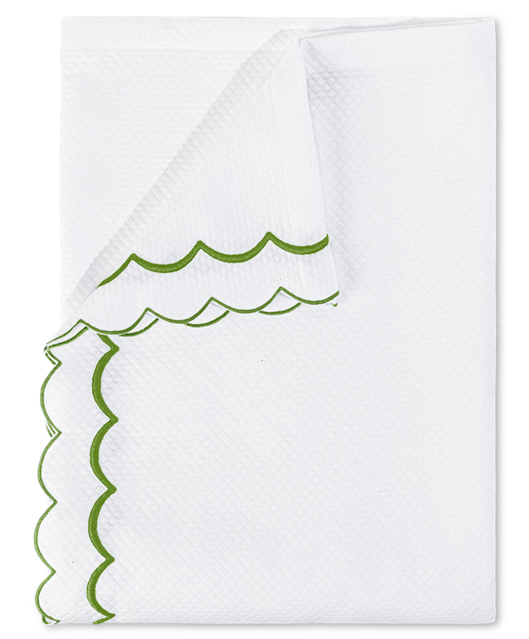 A folded white diamond pique napkin from the Matouk India Pique Bedding Collection in Grass, featuring green double-scallop embroidery along the textured edges.