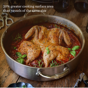 A roasted spatchcock chicken in tomato sauce sits in the Hestan Thomas Keller Commercial Clad Stainless Steel Rondeau, 6qt, garnished with fresh basil. The wide, shallow design offers increased cooking surface area and showcases premium craftsmanship.