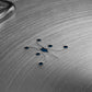 Close-up of the Hestan Commercial Clad Stainless Steel Universal Lid, 11", featuring six small circular holes and symmetrical engraved lines, with a blue background highlighting its sleek, space-saving design.
