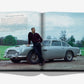 A man leans against a silver 1964 Aston Martin DB5, an iconic James Bond car, with grass and trees behind him, pictured inside the James Bond Cars book by Assouline.