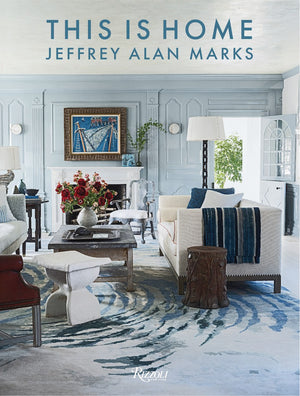The book "This Is Home" by Rizzoli showcases relaxed, refined interiors with a stylish living room, light blue walls, a fireplace, and modern furniture.