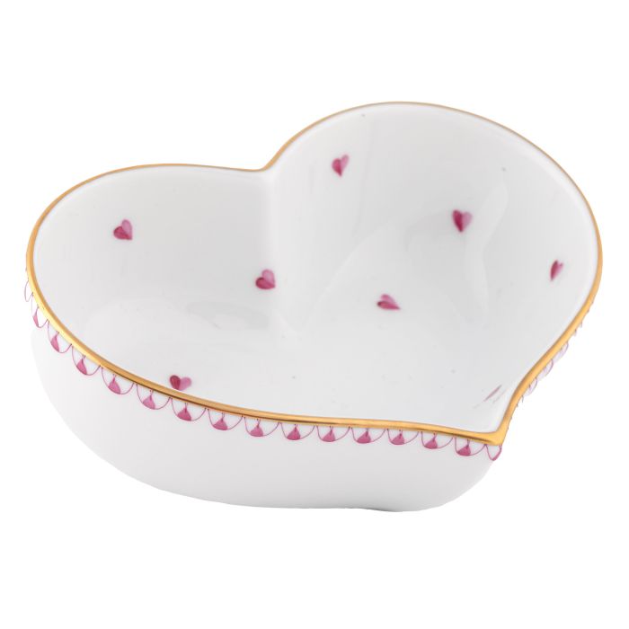 The Herend Heart Bowl is a white porcelain bowl shaped like a heart, adorned with hand-painted small pink hearts and finished with a gold-edged rim.