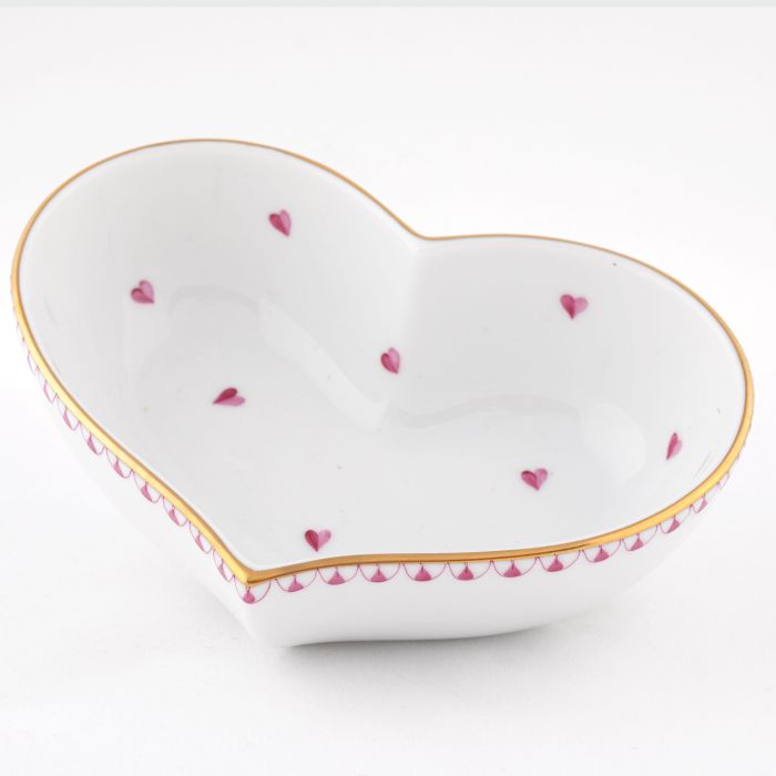 The Herend Heart Bowl is a white, heart-shaped ceramic dish with a gold rim and small pink hearts, featuring hand-painted designs for an artistic touch.