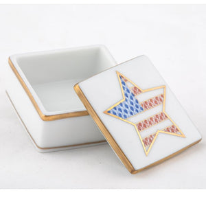 The Herend Patriotic Box is a small square white porcelain collectible with a removable lid, featuring a gold-bordered star adorned with an American flag pattern—a charming accent for any space.