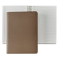 A 7" Leather Notebook by Graphic Image, a true writer's companion, rests atop an open spiral-bound lined notebook.