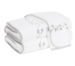 Two folded white towels from the Matouk Jasmine Giza Bath Collection in Cloud, featuring light gray edging and a subtle branch and blossom embroidery, crafted from plush Egyptian cotton terry for a luxurious bathroom experience.