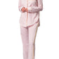 A person stands barefoot against a white background, wearing Matouk's Jasper Pajama Set in light pink cotton sateen with yellow piping.