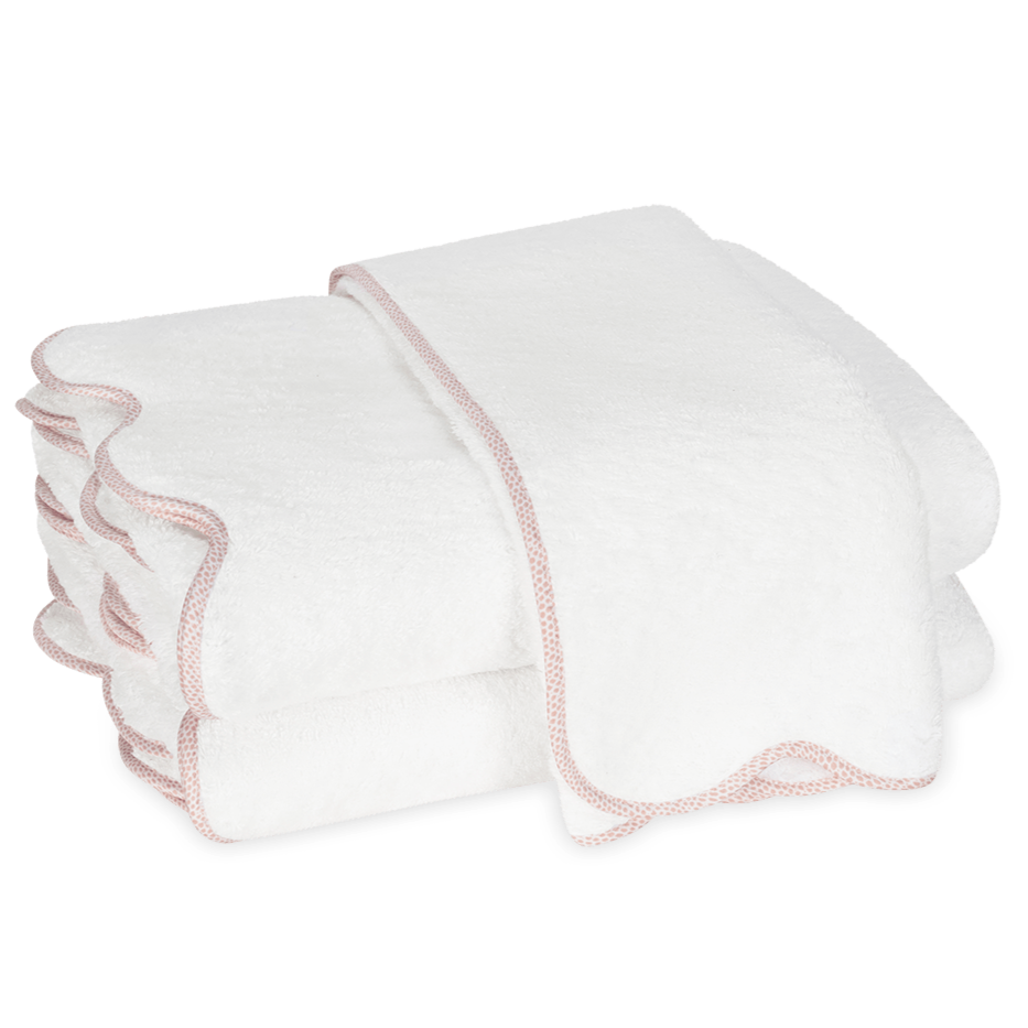 Two white towels with light pink scalloped edges from the Matouk Jasper Bath Collection are stacked against a plain background.