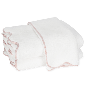 Two white towels with light pink scalloped edges from the Matouk Jasper Bath Collection are stacked against a plain background.