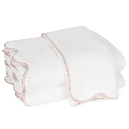 Two white towels with light pink scalloped edges from the Matouk Jasper Bath Collection are stacked against a plain background.