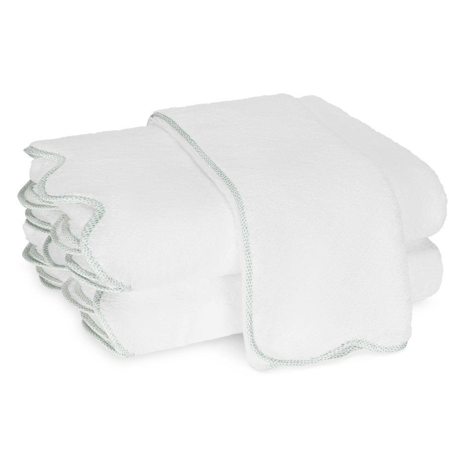 Two neatly folded white towels from the Matouk Jasper Bath Collection, with scalloped edges and subtle trim, are stacked atop one another against a plain background.