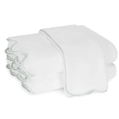 Two neatly folded white towels from the Matouk Jasper Bath Collection, with scalloped edges and subtle trim, are stacked atop one another against a plain background.