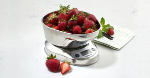 A Cuisinart PrecisionChef Bowl Digital Kitchen Scale with a stainless steel bowl of fresh strawberries rests on a white surface, next to a green-striped cloth.