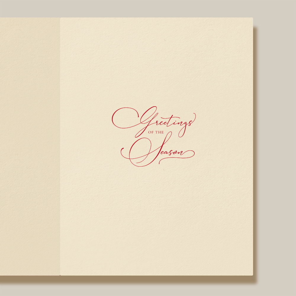 The Christmas Morning Wreath Card Set by Crane features an open cream-colored card with "Greetings of the Season" in red cursive at the center, framed by a delicate wreath design.