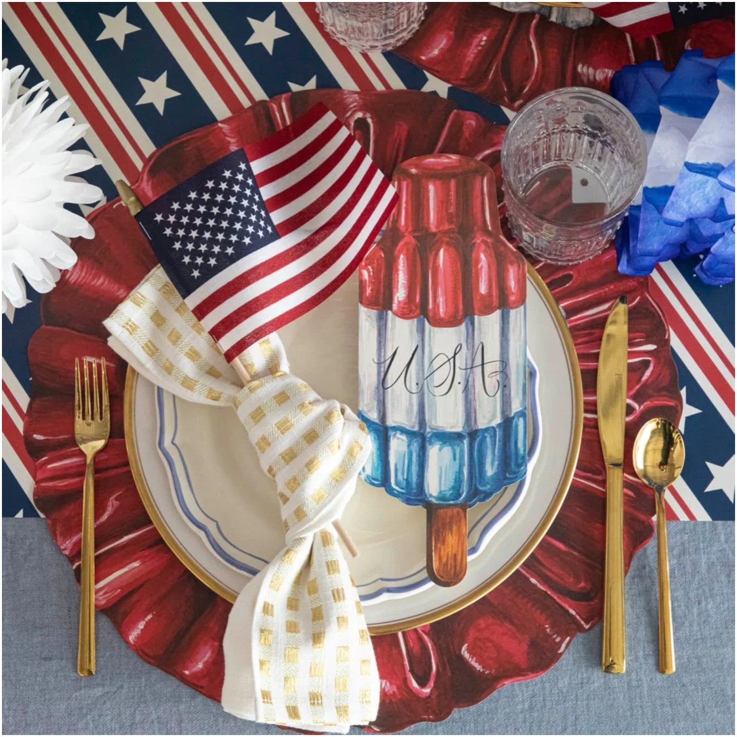 Create a patriotic table setting with Hester & Cook’s Star Spangled Paper Placemats, gold flatware, flag napkins, and glasses on a USA-striped tablecloth—perfect for summer barbecues or picnic gatherings.