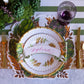 The Autumnal Artichoke decorative plate by Hester & Cook is set with gold utensils and a glass filled with purple liquid; warm fall colors enhance the scene, while a name card labeled “Sylvia” sits atop the plate.