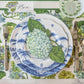 A table set with blue and white plates, silver cutlery, a green glass, and a floral placemat from Hester & Cook’s Hydrangea Collection features a hydrangea accent and a place card labeled "Ben" for an elegant setting.