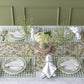 A spring-inspired table setting with a classic touch, featuring Hester & Cook Dark Green Painted Check Rectangle Placemats, floral “Charlotte” and “Jennifer” plates, crisp white napkins, elegant glassware, and a white hydrangea centerpiece.