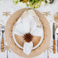 A table setting with bamboo-style flatware, wooden charger, white plate, and an embroidered napkin folded with the Kim Seybert Florette Brown Napkin Ring—ideal for outdoor gatherings and accented with palm tree motifs.